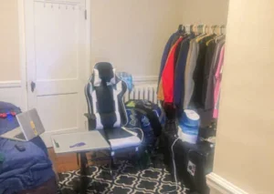 A gaming chair with a laptop on a small table beside a bed