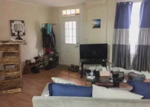 A living room with a blue and white couch, TV and coffee table. The room has a wooden floor and a window with curtains.