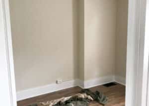 A room corner with wood flooring and beige walls. The baseboards are white.