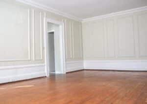 An empty room with a shiny wood floor and white walls featuring decorative trim. The room has a doorway leading to another room.
